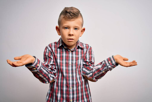 Young little caucasian kid with blue eyes wearing elegant shirt standing over isolated background clueless and confused with open arms, no idea concept. - Photo, Image
