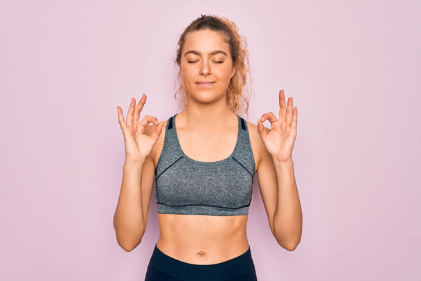Young beautiful blonde sportswoman with blue eyes doing exercise wearing sportswear relaxed and smiling with eyes closed doing meditation gesture with fingers. Yoga concept. - Photo, Image