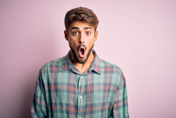 Young handsome man with beard wearing casual shirt standing over pink background afraid and shocked with surprise expression, fear and excited face. - Foto, Bild