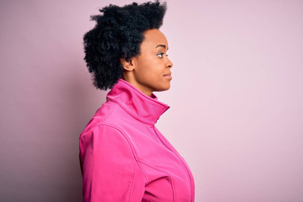 Junge afroamerikanische Afro-Sportlerin mit lockigem Haar trägt Sportbekleidung doin sport, die zur Seite schaut, entspannte Profil-Pose mit natürlichem Gesicht mit selbstbewusstem Lächeln. - Foto, Bild