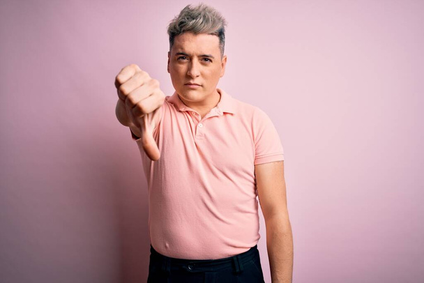 Giovane bell'uomo moderno indossa casual t-shirt rosa su sfondo isolato cercando infelice e arrabbiato mostrando rifiuto e negativo con i pollici verso il basso gesto. Cattiva espressione
. - Foto, immagini