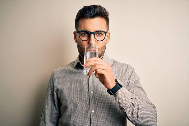 眼鏡とシャツを着た若いハンサムなビジネスマン。健康的な水のグラスを立って孤立した白い背景の上にリフレッシュする - 写真・画像