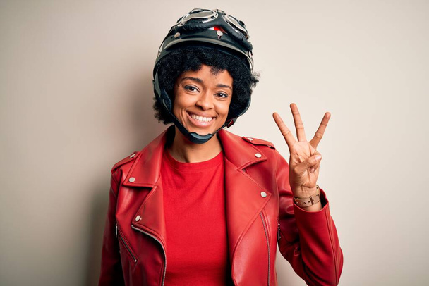 Young African American afro motorcyclist woman with curly hair wearing motorcycle helmet showing and pointing up with fingers number three while smiling confident and happy. - Photo, Image