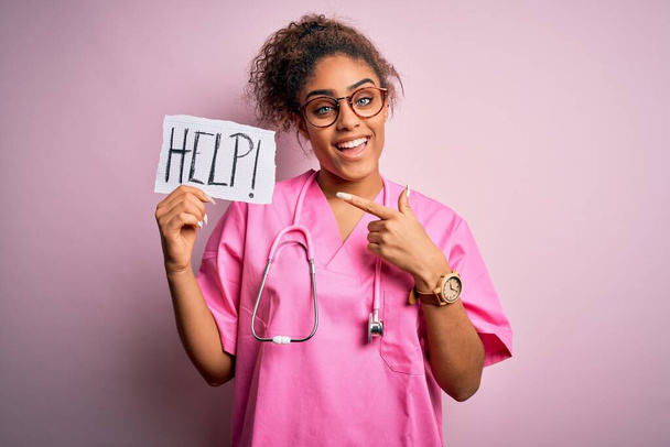African american doctor girl wearing medical uniform and stethoscope holding help paper very happy pointing with hand and finger - Photo, Image