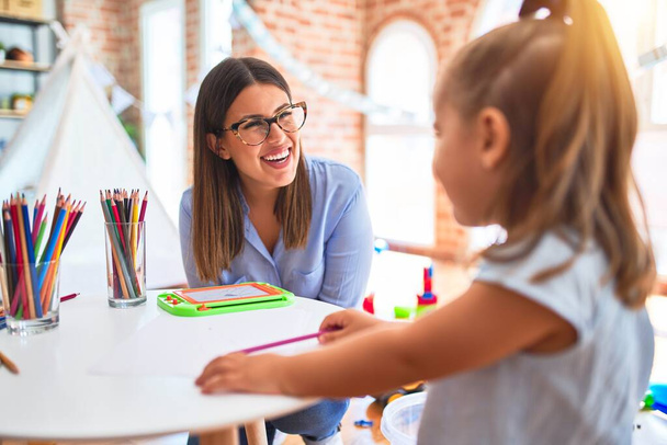 Biała dziewczynka bawiąca się i ucząca w przedszkolu z nauczycielką. Matka i córka w pokoju zabaw wokół zabawek rysunek w kolorach ołówka - Zdjęcie, obraz