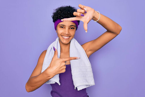 Kaunis afrikkalainen amerikkalainen urheilullinen nainen tekee urheilua yllään pyyhe violetti tausta hymyilevä tehdä runko kädet ja sormet onnellinen kasvot. Luovuus ja valokuvaus käsite
. - Valokuva, kuva