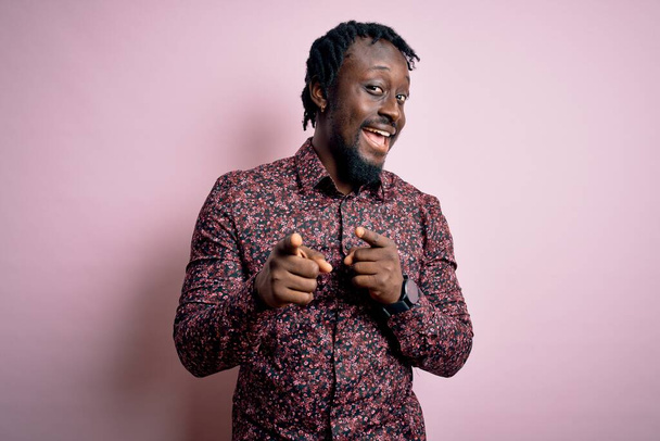 Junger gutaussehender afrikanisch-amerikanischer Mann in lässigem Hemd, das über rosa Hintergrund steht und mit dem Finger in die Kamera zeigt, mit fröhlichem und lustigem Gesicht. Gute Energie und Stimmung. - Foto, Bild