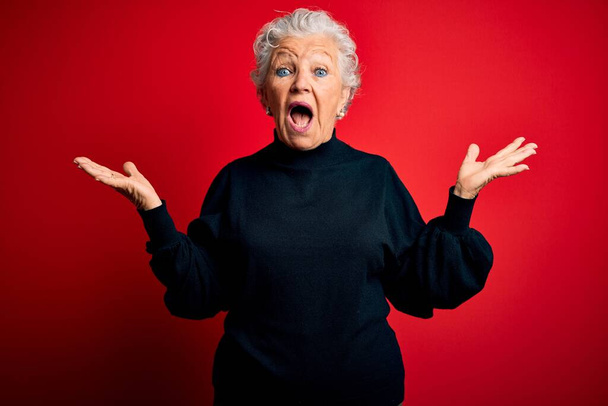 Senior beautiful woman wearing casual sweater standing over isolated red background celebrating crazy and amazed for success with arms raised and open eyes screaming excited. Winner concept - Fotografie, Obrázek