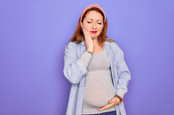Młoda piękna ruda kobieta w ciąży spodziewa się dziecka na odizolowanym fioletowym tle dotykając ust z bolesnym wyrazem twarzy z powodu bólu zęba lub choroby zębów na zębach. Dentysta - Zdjęcie, obraz