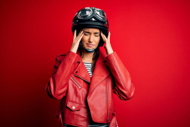 Young beautiful brunette motorcyclist woman wearing motorcycle helmet and red jacket suffering from headache desperate and stressed because pain and migraine. Hands on head. - Фото, изображение