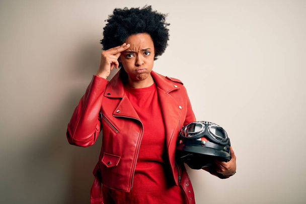 Joven afroamericana afro motociclista mujer con el pelo rizado celebración de casco de la motocicleta preocupado y estresado por un problema con la mano en la frente, nervioso y ansioso por la crisis - Foto, Imagen