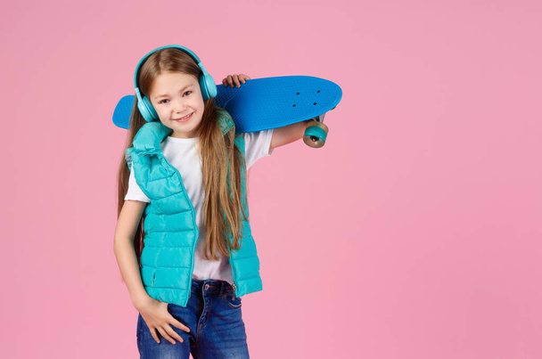 Beautiful little blonde kid girl 7-10 years old in jacket posing isolated on pastel pink background children portrait. Childhood lifestyle concept. Mock up copy space. Hold blue skateboard - Φωτογραφία, εικόνα