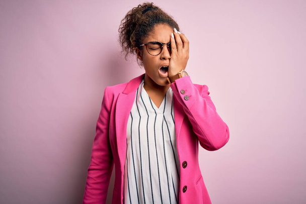 Schöne afrikanisch-amerikanische Geschäftsfrau trägt Jacke und Brille über rosa Hintergrund Gähnende Müdigkeit bedeckt das halbe Gesicht, Augen und Mund mit der Hand. Gesicht schmerzt vor Schmerzen. - Foto, Bild