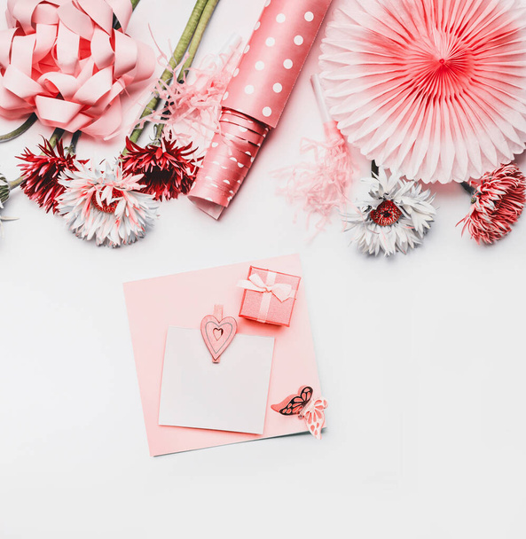 Female still life greeting objects in coral color on white background with greeting card mock up. Ribbon , paper party fan, flowers and dotted wrapping paper on white background.  Flat lay, top view. - Фото, изображение