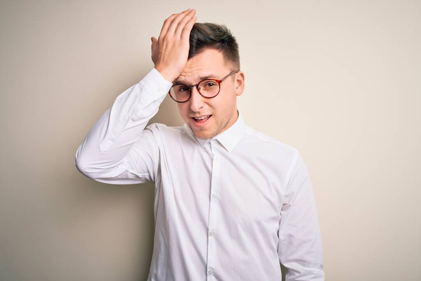 Young handsome business mas wearing glasses and elegant shirt over isolated background surprised with hand on head for mistake, remember error. Forgot, bad memory concept. - Фото, изображение