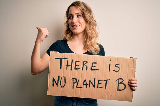 Giovane donna bionda attivista che chiede l'ambiente tenendo banner con messaggio del pianeta che punta e mostra con il pollice verso l'alto sul lato con il viso felice sorridente
 - Foto, immagini