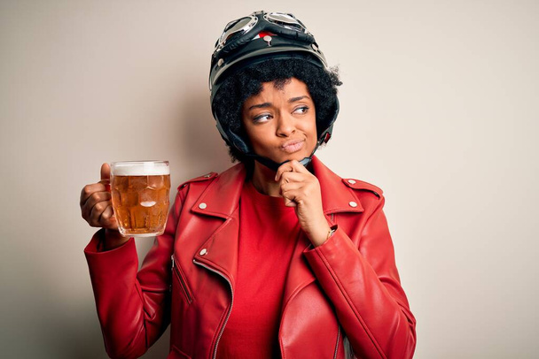 Joven afroamericana afro motociclista mujer con pelo rizado bebiendo tarro de cerveza cara seria pensando en la pregunta, idea muy confusa - Foto, Imagen