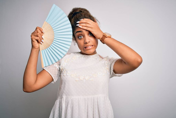 Young african american girl using hand fan to refreshment over isolated white background stressed with hand on head, shocked with shame and surprise face, angry and frustrated. Fear and upset for mistake. - Zdjęcie, obraz
