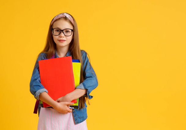 portrait of happy caucasian school girl with a book. beautiful positive girl with long red hair stand and hug her book, look at camera. she is preparing to school . isolated yellow background - Φωτογραφία, εικόνα