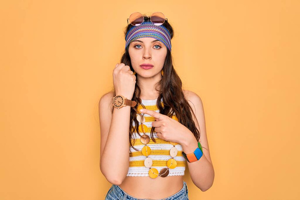 Young beautiful hippie woman with blue eyes wearing accesories and sunnglasses In hurry pointing to watch time, impatience, looking at the camera with relaxed expression - Foto, imagen