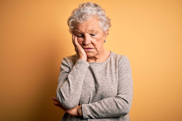 Senior beautiful woman wearing casual t-shirt standing over isolated yellow background thinking looking tired and bored with depression problems with crossed arms. - Fotó, kép
