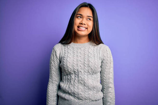 Young beautiful asian girl wearing casual sweater standing over isolated purple background looking away to side with smile on face, natural expression. Laughing confident. - Foto, immagini