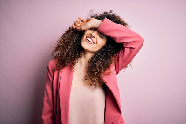 Young beautiful businesswoman with curly hair and piercing wearing elegant jacket covering eyes with arm smiling cheerful and funny. Blind concept. - Photo, Image
