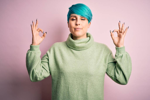 Young beautiful woman with blue fashion hair wearing casual turtleneck sweater relax and smiling with eyes closed doing meditation gesture with fingers. Yoga concept. - Foto, afbeelding