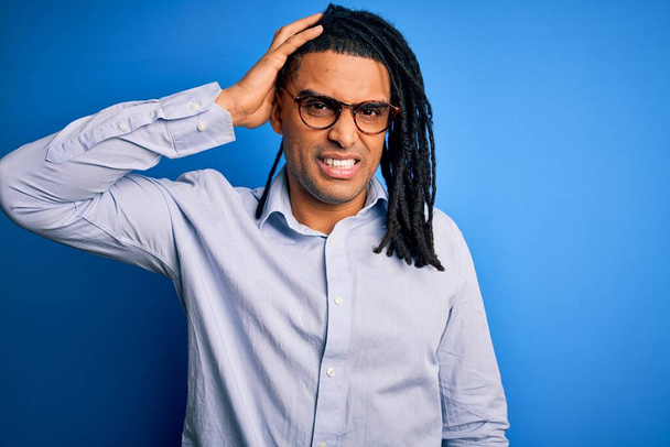 Young handsome african american man with dreadlocks wearing casual shirt and glasses confuse and wonder about question. Uncertain with doubt, thinking with hand on head. Pensive concept. - Valokuva, kuva