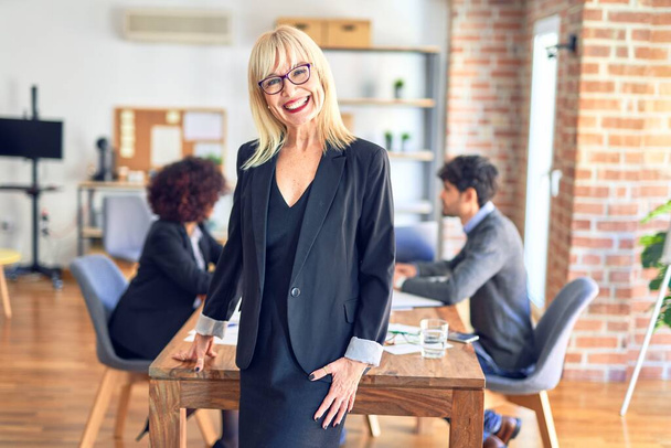 Группа бизнес-работников, работающих вместе. Красивая женщина средних лет, улыбающаяся, счастливая, глядя на камеру в офисе
 - Фото, изображение