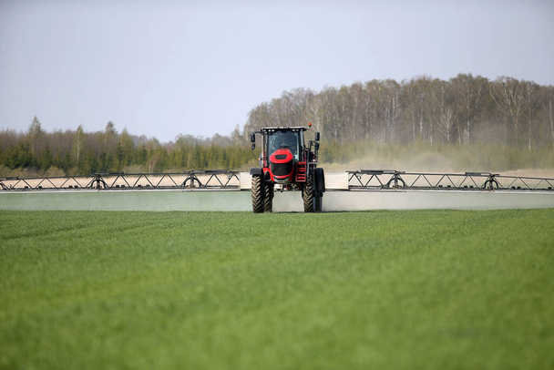 Трактор опрыскивает пшеничное поле опрыскивателем
 - Фото, изображение