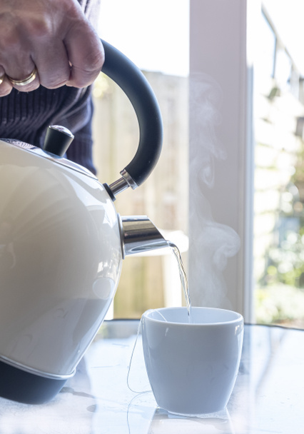 Електричний чайник з киплячою водою для трав'яного чаю, чоловіча рука, яка вливає воду в чашку чаю. Селектив зосереджений на чайнику і залитий te
 - Фото, зображення
