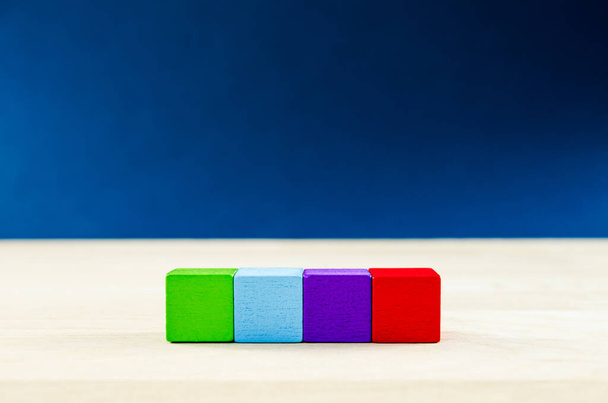 4 colored wooden blocks placed in a row, with copy space, over blue background. - Photo, Image
