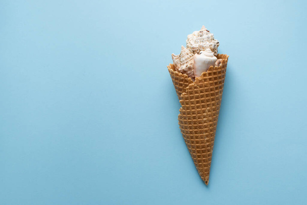 Creative composition with seashell and ice cream cone on pastel blue background. Summer minimal concept. Collection of seashells in waffle horn. Stylized ice cream. Vacation flat lay. Copy space. - Foto, Imagem
