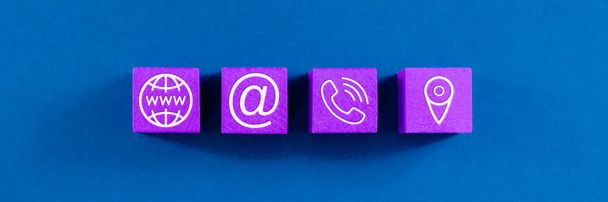 Ampia visualizzazione dell'immagine del servizio clienti con quattro dadi di legno con www, informazioni di contatto e icone di posizione su di loro. Su sfondo blu
. - Foto, immagini