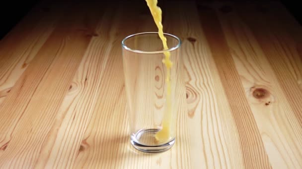 Glass goblet on a wooden table. A stream of orange juice with spray. Slow motion - Video