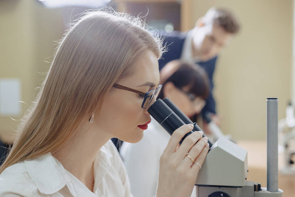 two girls and a boy work with microscopes at laboratory - Photo, Image