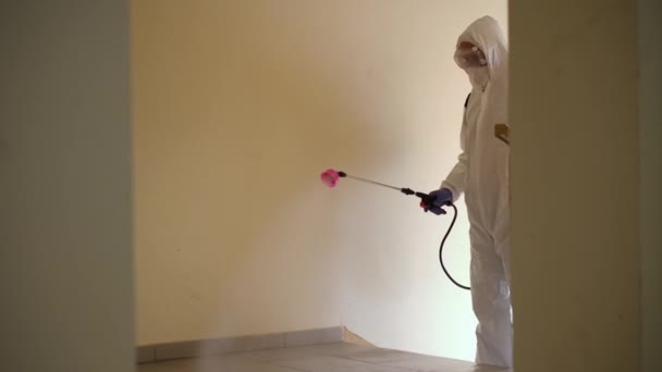 Egy védőfelszerelésben lévő férfi fertőtlenít egy sprayvel az épületben. Koronavírus covid-19 betegség miatti felületkezelés. Egy fehér öltönyös férfi fertőtleníti a házat egy szórópisztollyal. Vírusjárvány - Felvétel, videó