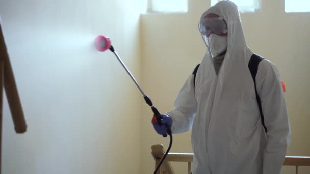 Ein Mann in Schutzausrüstung desinfiziert sich im Gebäude mit einem Spray. Oberflächenbehandlung wegen Coronavirus covid-19 Krankheit. Ein Mann im weißen Anzug desinfiziert das Haus mit einer Spritzpistole. Virus-Pandemie - Filmmaterial, Video