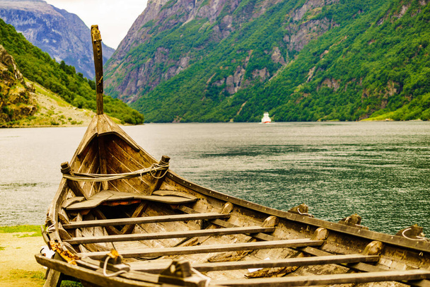 Old wooden viking boat on seashore in norwegian nature and ferryboat on fjord. Mountains and Sognefjord. Tourism and traveling concept - Valokuva, kuva