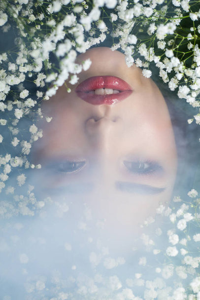 Portrait of beautiful girl in smoke with small white flowers around her face. Woman and flowers. Spring. - 写真・画像