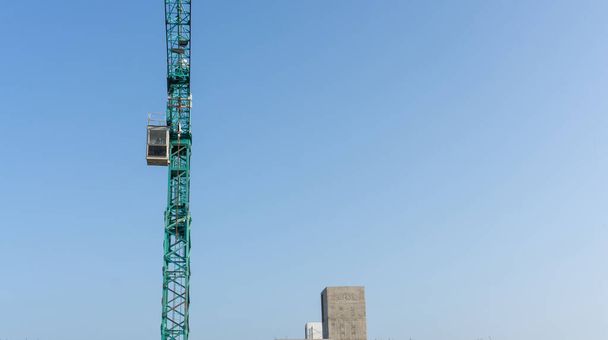 Vista verso l'alto della grande gru a torre alta, macchina in movimento e costruzione in lavori di costruzione, impalcatura all'ultimo piano, sotto bianco soffice nuvola cielo blu chiaro
 - Foto, immagini