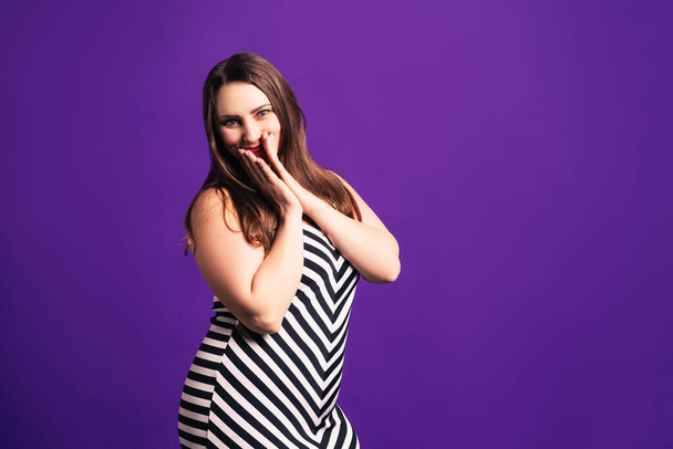 Happy plus size model in striped dress, fat woman on purple background, body positive concept - Foto, imagen