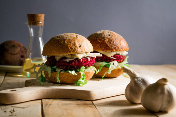 Veganistische hamburger van bietenfalafel. Veganistische hamburger met een roze karbonade, verse salade en mayonaise van sojamelk op een houten achtergrond. Falafel in de vorm van een hart - Foto, afbeelding