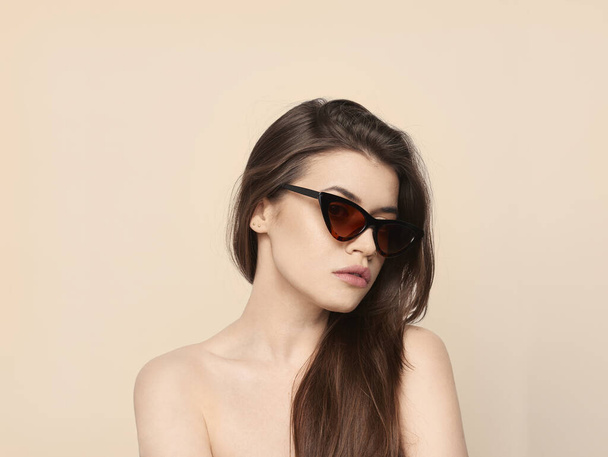beautiful young girl with brown hair in fashionable glasses posing on a yellow background with bare shoulders, empty space for text - Photo, Image