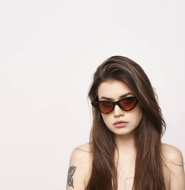 beautiful young girl with brown hair in fashionable glasses posing on a white background with bare shoulders, empty space for text - Photo, Image