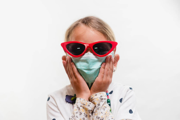 Little blond girl wearing disposable mask and sunglasses over white background - Fotoğraf, Görsel