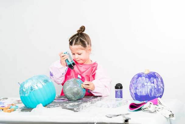 Bambina che decora la sua zucca di Halloween con glitter in tema sirena. - Foto, immagini