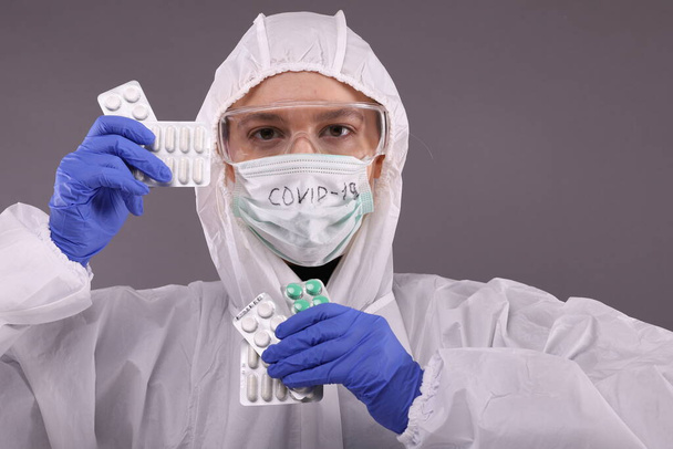 Woman in protective costume and mask with "COVID-19" sign holds a syringe - Фото, изображение