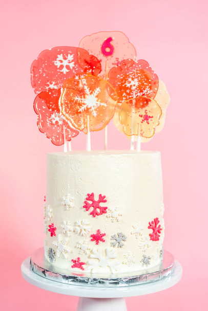 Bolo alto redondo com cobertura de creme de manteiga italiano decorado com flocos de neve fondant e coberto com grandes pirulitos rosa e branco no fundo rosa. - Foto, Imagem